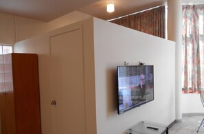 Une pièce avec un téléviseur fixé au mur, une armoire en bois et une fenêtre avec des rideaux.