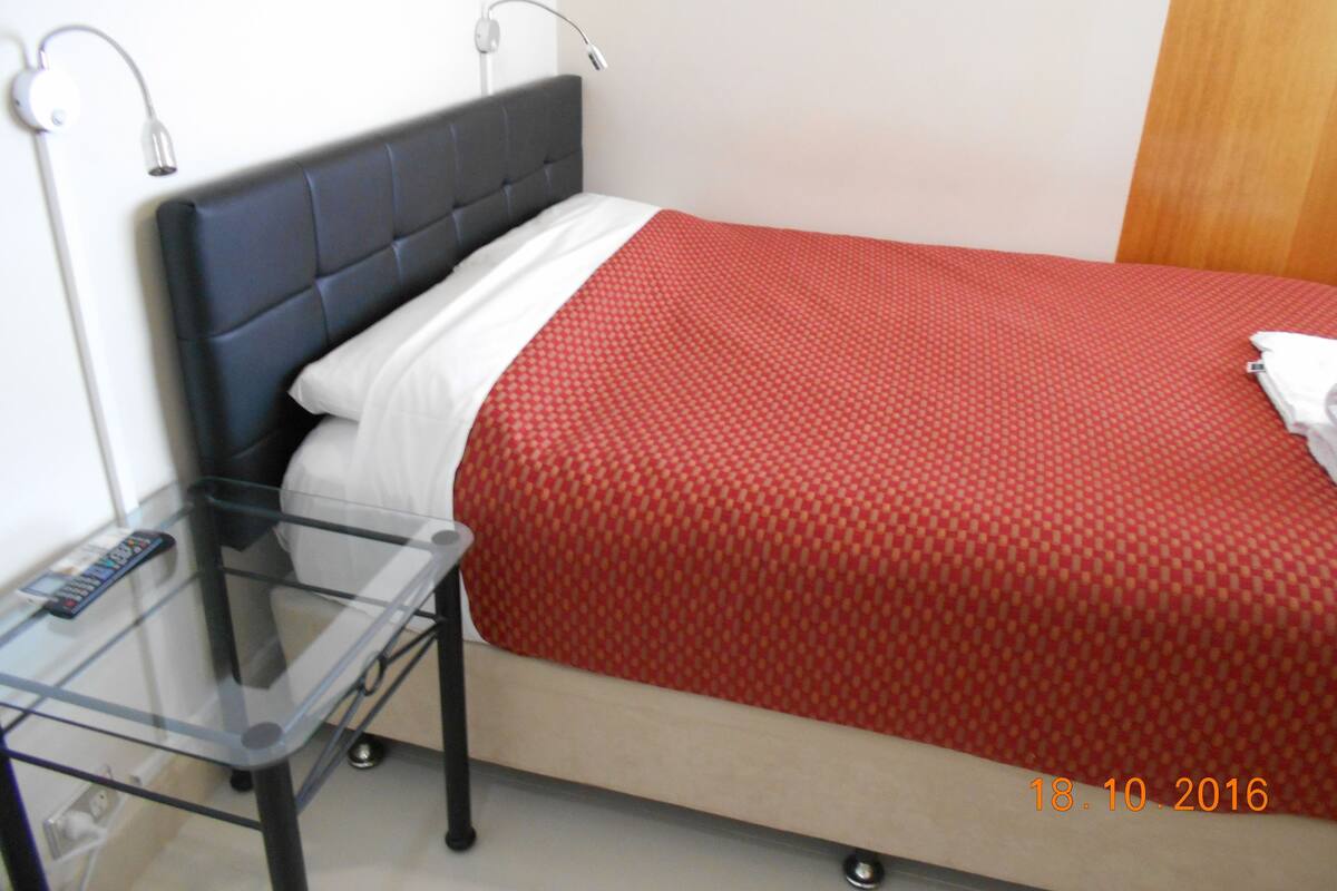 Une petite chambre d’hôtel avec un lit simple, une table en verre et une télécommande posée sur la table.