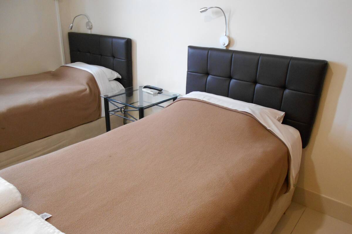 Une chambre d’hôtel avec deux lits simples, chacun doté d’une tête de lit et d’une table de chevet.