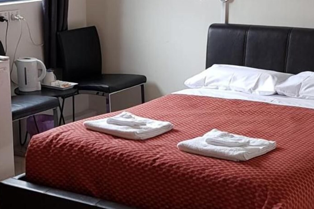 A hotel room with a bed, a desk with a chair, a coffee maker, and a small refrigerator.
