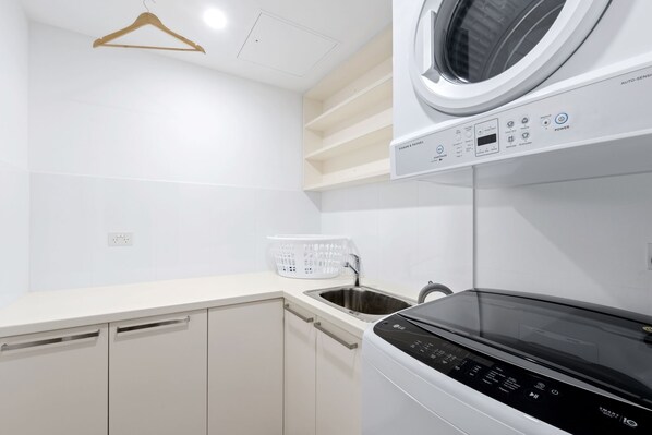 A modern laundry room with a front-loading washer and dryer, a stainless steel sink, and a drying rack.