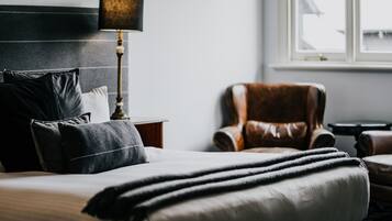 A neatly made bed with a black and white striped blanket, a leather armchair, and a lamp on a bedside table in a hotel room.