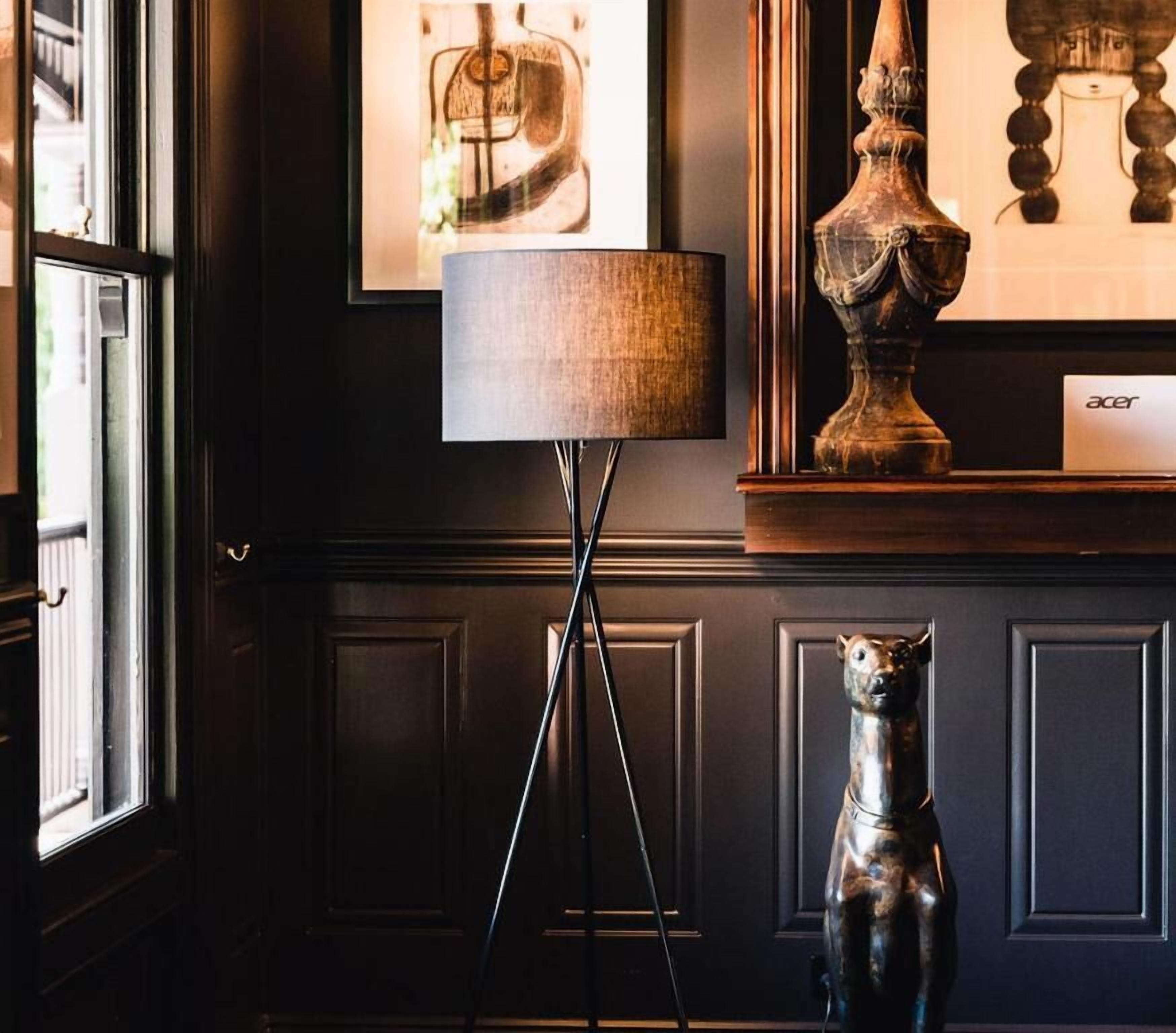Een kamer met een lamp, een sculptuur en kunstwerken in lijsten aan de muur.