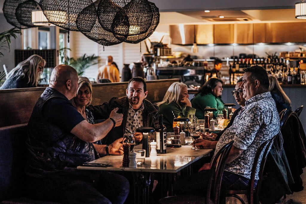 A group of people seated at a table in a restaurant with a bar in the background.