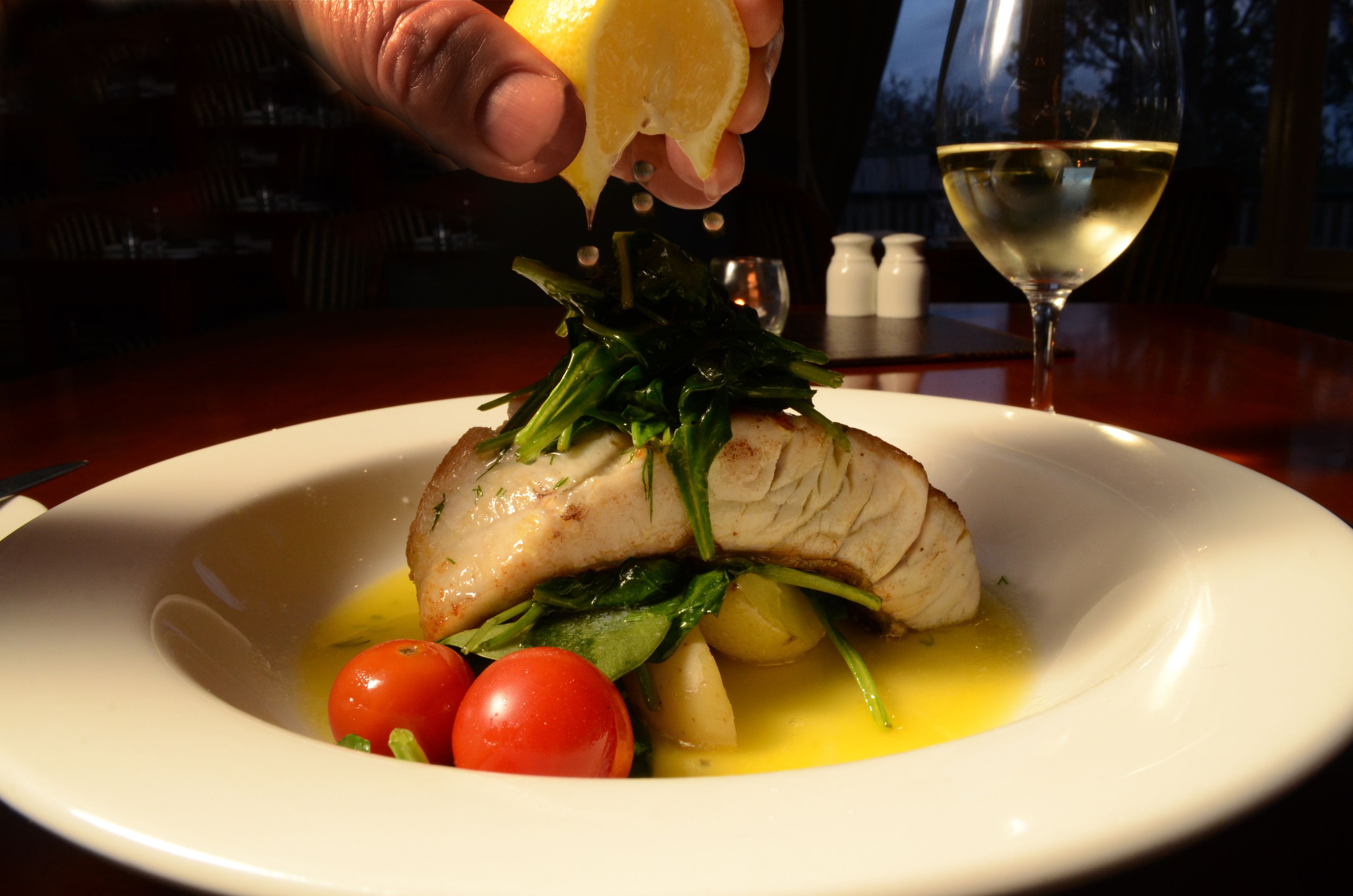 Um prato com peixe, tomate cereja e vegetais, com um limão sendo espremido por cima.