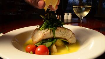 A plate with a fish, cherry tomatoes, and greens, with a lemon being squeezed over it.