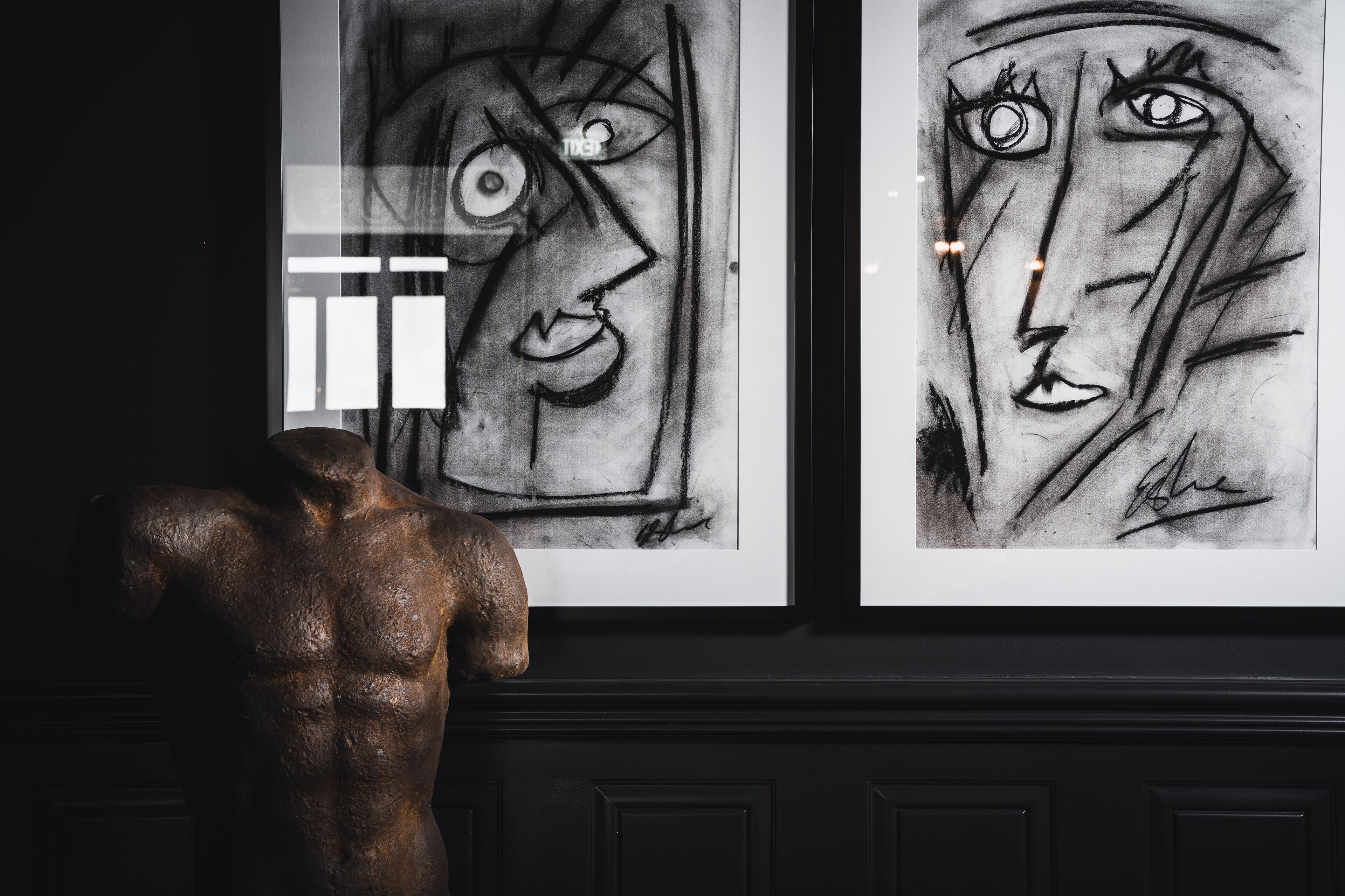 A sculpture of a muscular figure next to two framed artworks on a wall.
