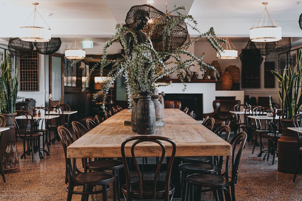 A spacious dining area with a long wooden table surrounded by chairs, a decorative centerpiece, and hanging pendant lights.