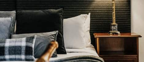 Una cama bien hecha con un cabecero oscuro, una lámpara de noche y una mesita de noche de madera con cajones.