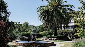 Un jardin aménagé avec une fontaine circulaire en pierre, des palmiers et un bâtiment en arrière-plan.