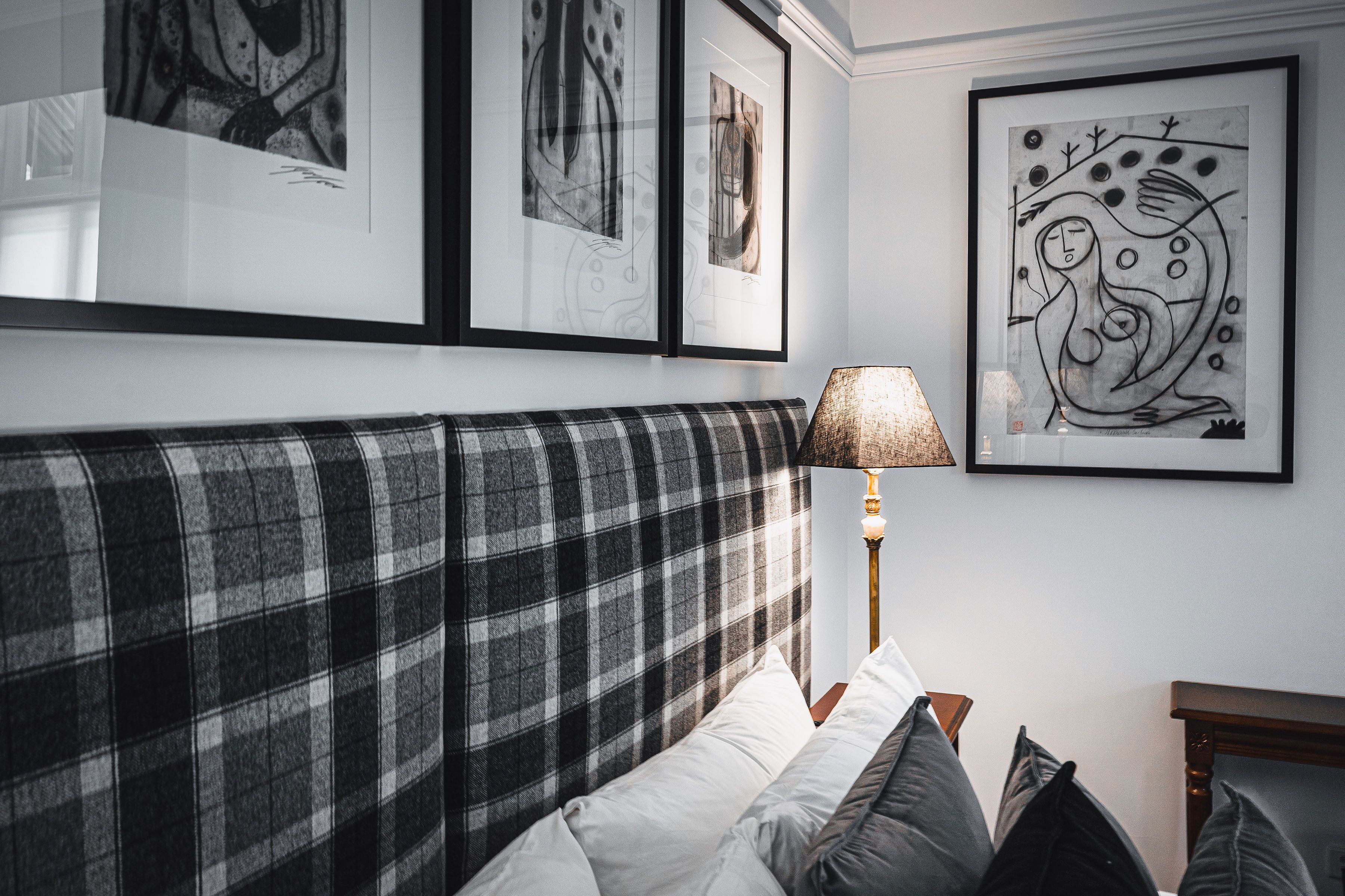 A neatly arranged bedroom with a plaid headboard, a bedside lamp, and framed artwork on the wall.