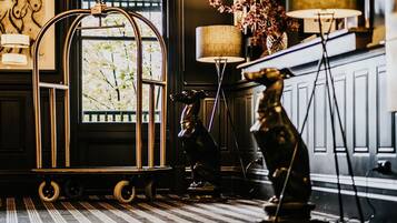 A vintage-style room with a large window, a decorative birdcage on wheels, a statue, and a floor lamp.