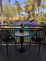 Zona junto a la piscina con dos sillas, una mesa, una piscina y palmeras al fondo.