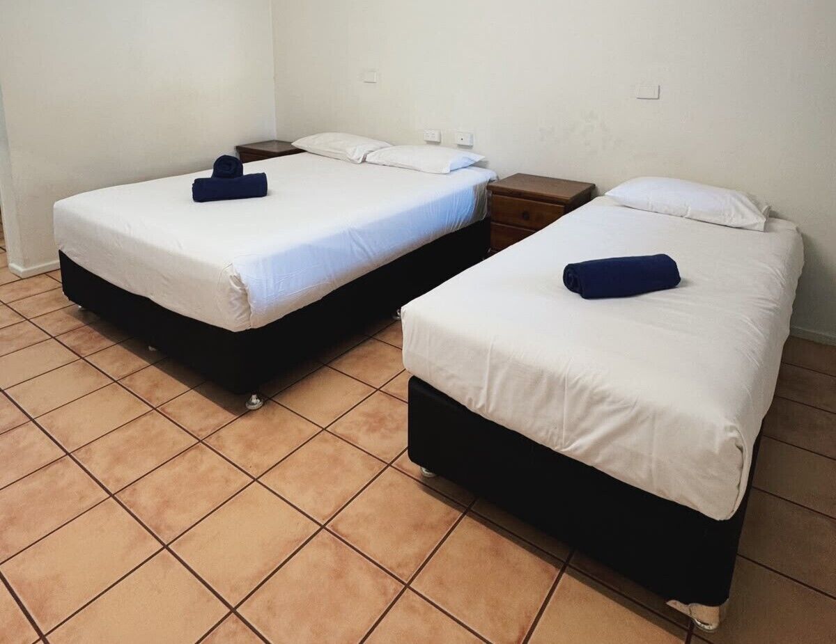Two single beds with white bedding and dark headboards, a wooden nightstand, and a tiled floor.