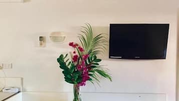 Un coin repas avec une table blanche, des chaises en osier, un vase avec des fleurs, un climatiseur mural et un téléviseur à écran plat.