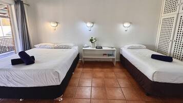 Ein Hotelzimmer mit zwei Betten, einem kleinen Nachttisch, einer Wandleuchte und Blick ins Freie.
