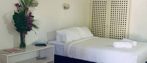 Une chambre d’hôtel avec deux lits, une table de chevet, une lampe fixée au mur et une plante décorative.