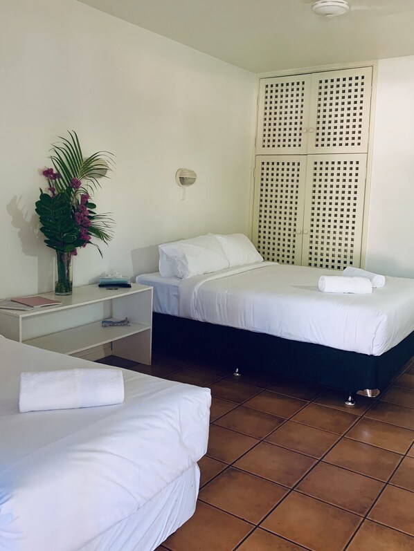 A hotel room with two beds, a nightstand, a wall-mounted light, and a decorative plant. - Roebuck Bay Hotel (Broome)
