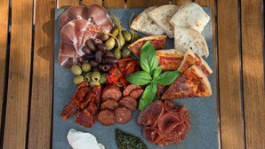 Una tabla de embutidos con diferentes carnes, aceitunas y pan sobre una tabla de pizarra.