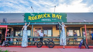 Hotel Roebuck Bay con letrero verde, mesas al aire libre y una bicicleta.