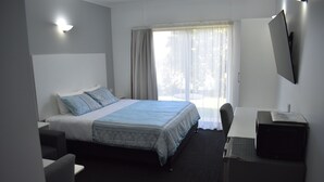 A hotel room with a bed, a desk, a chair, a TV, and a window with curtains.