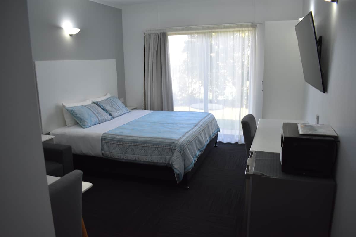 Une chambre d’hôtel avec un lit, un bureau, une chaise, une télévision et une fenêtre avec des rideaux.