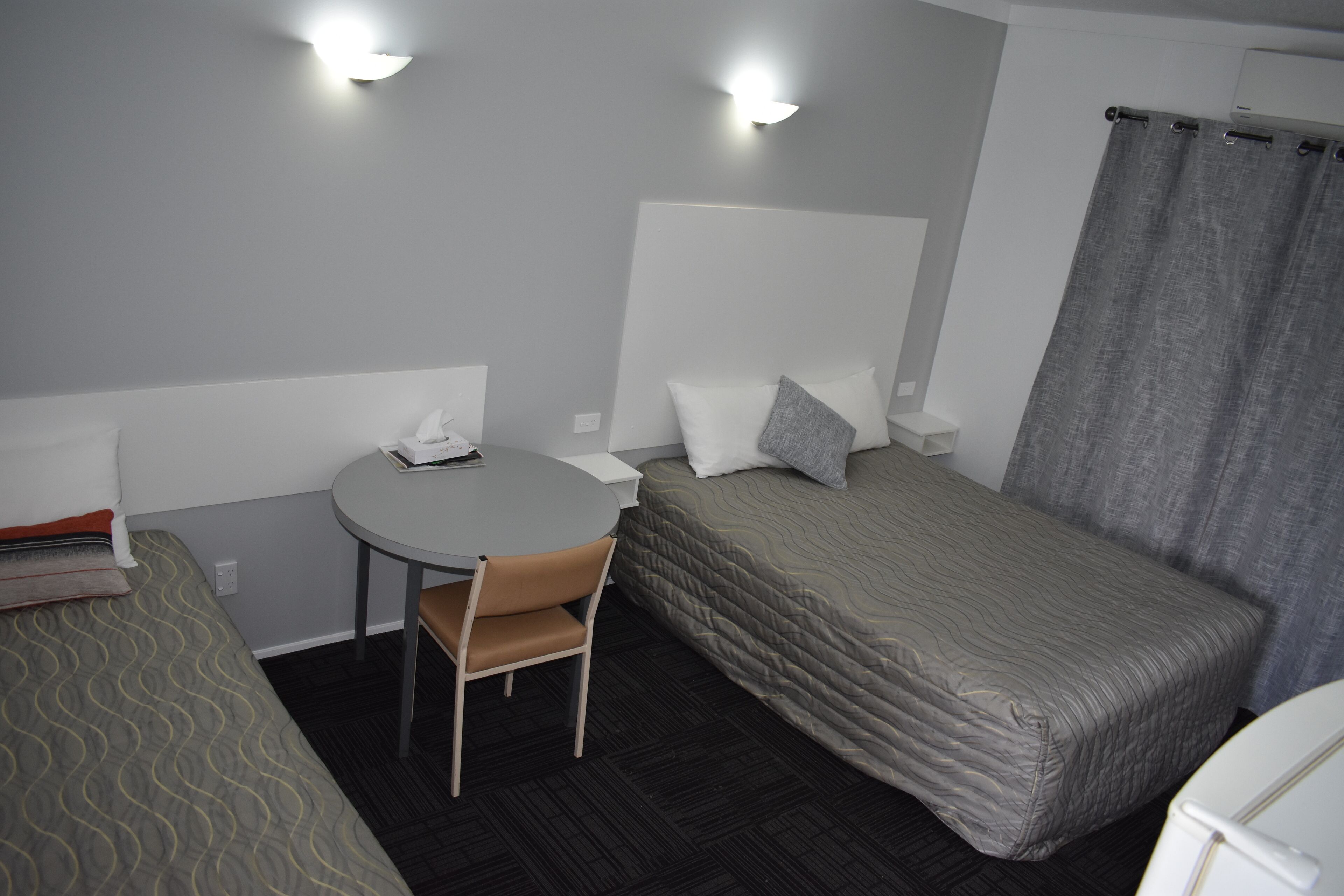 Een kleine hotelkamer met een enkel bed, een klein rond tafeltje, een stoel en een bureau.