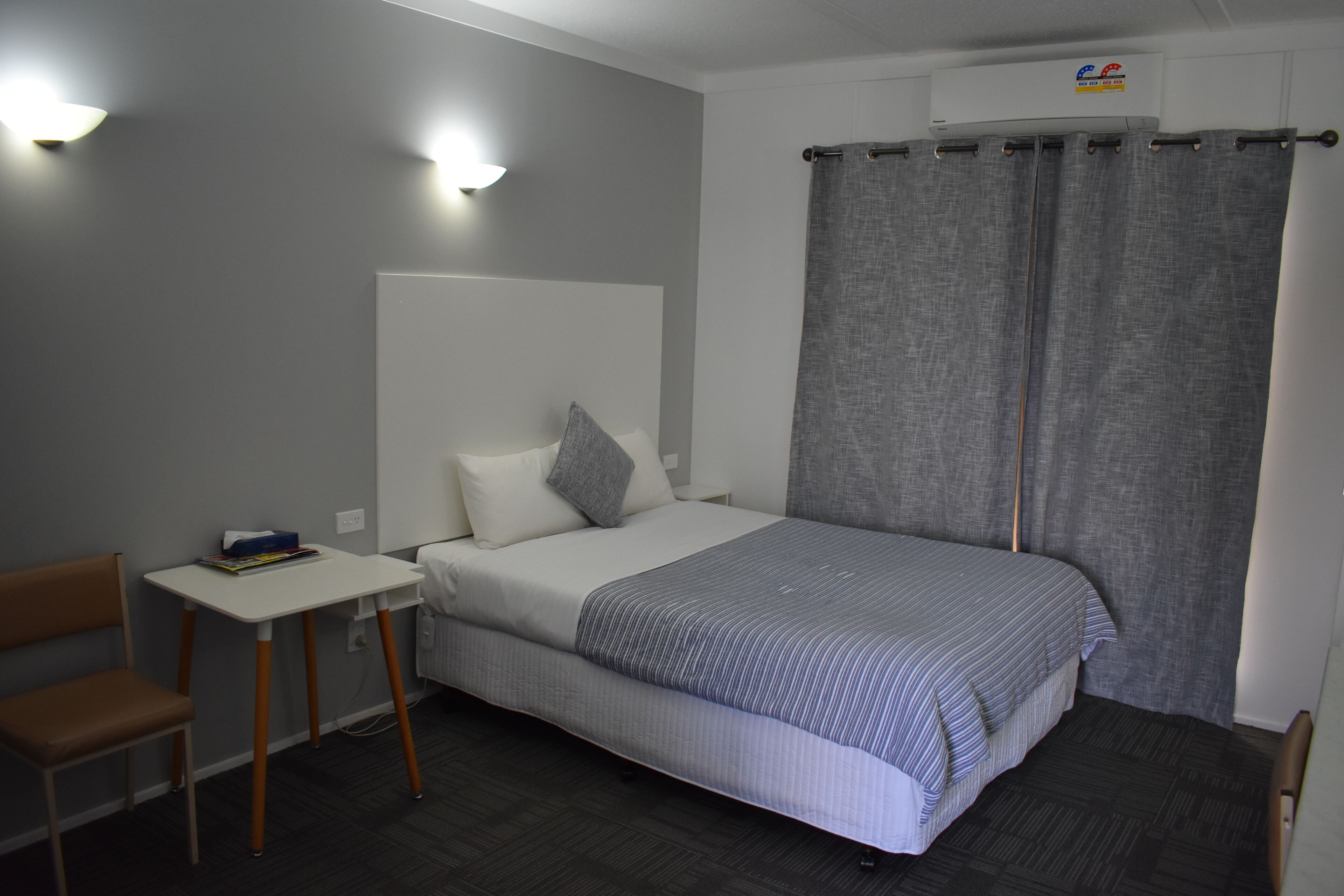 Ein Schlafzimmer mit einem Bett, einem kleinen Tisch, einem Stuhl und einer Klimaanlage.