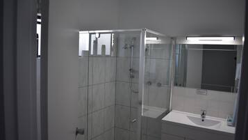 Un baño moderno con ducha de vidrio, lavamanos blanco y un espejo grande.