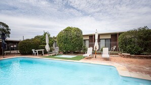 A swimming pool with lounge chairs and umbrellas, surrounded by a brick patio and greenery.