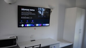 A kitchenette with a microwave, a small fridge, a cabinet, and a TV mounted on the wall displaying a series menu.