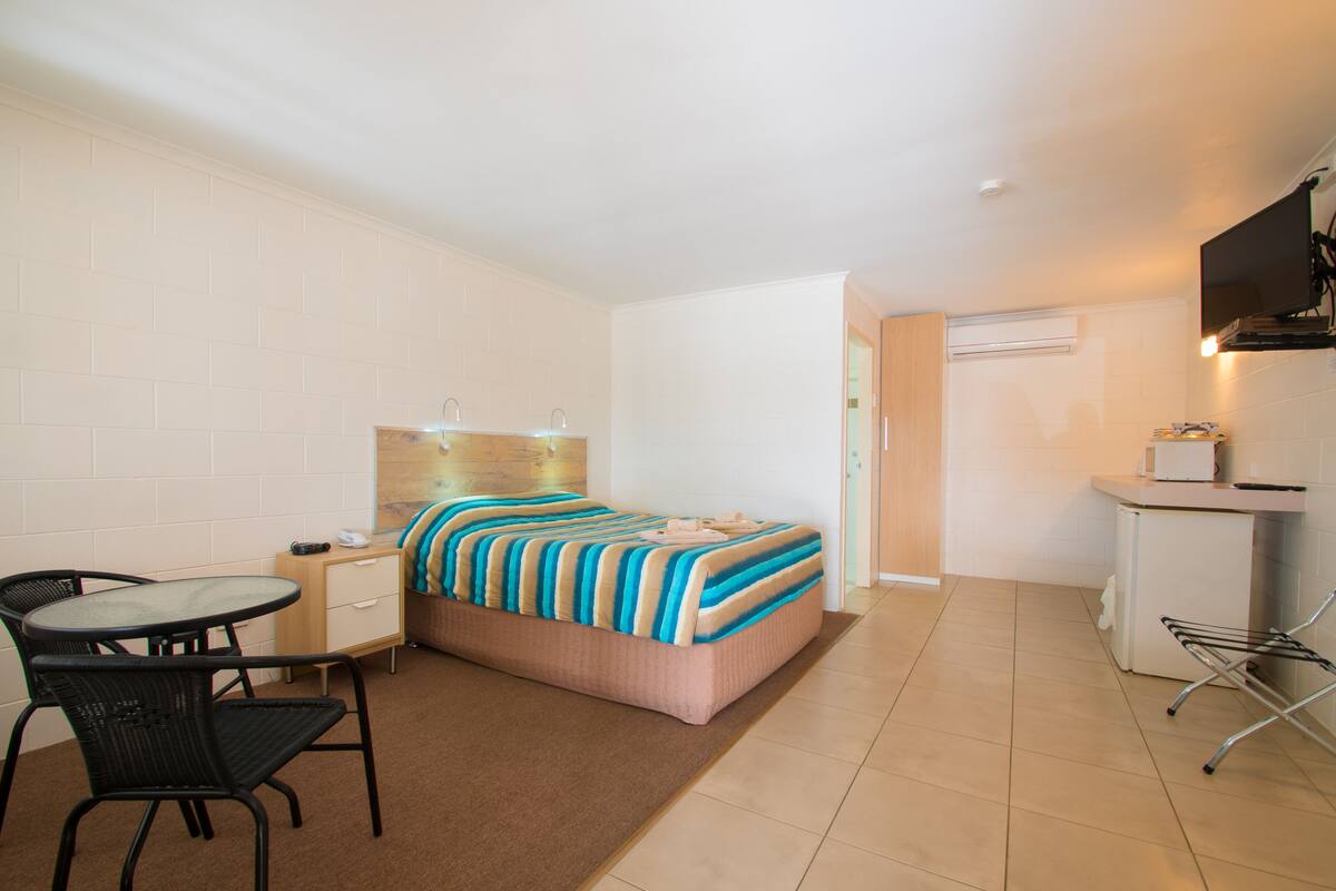Une chambre d’hôtel de taille réduite, comprenant un lit, un petit bureau, une chaise et une kitchenette.