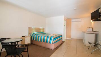 Ein kleines Hotelzimmer mit Bett, Schreibtisch, Stuhl und einer Küchenzeile.