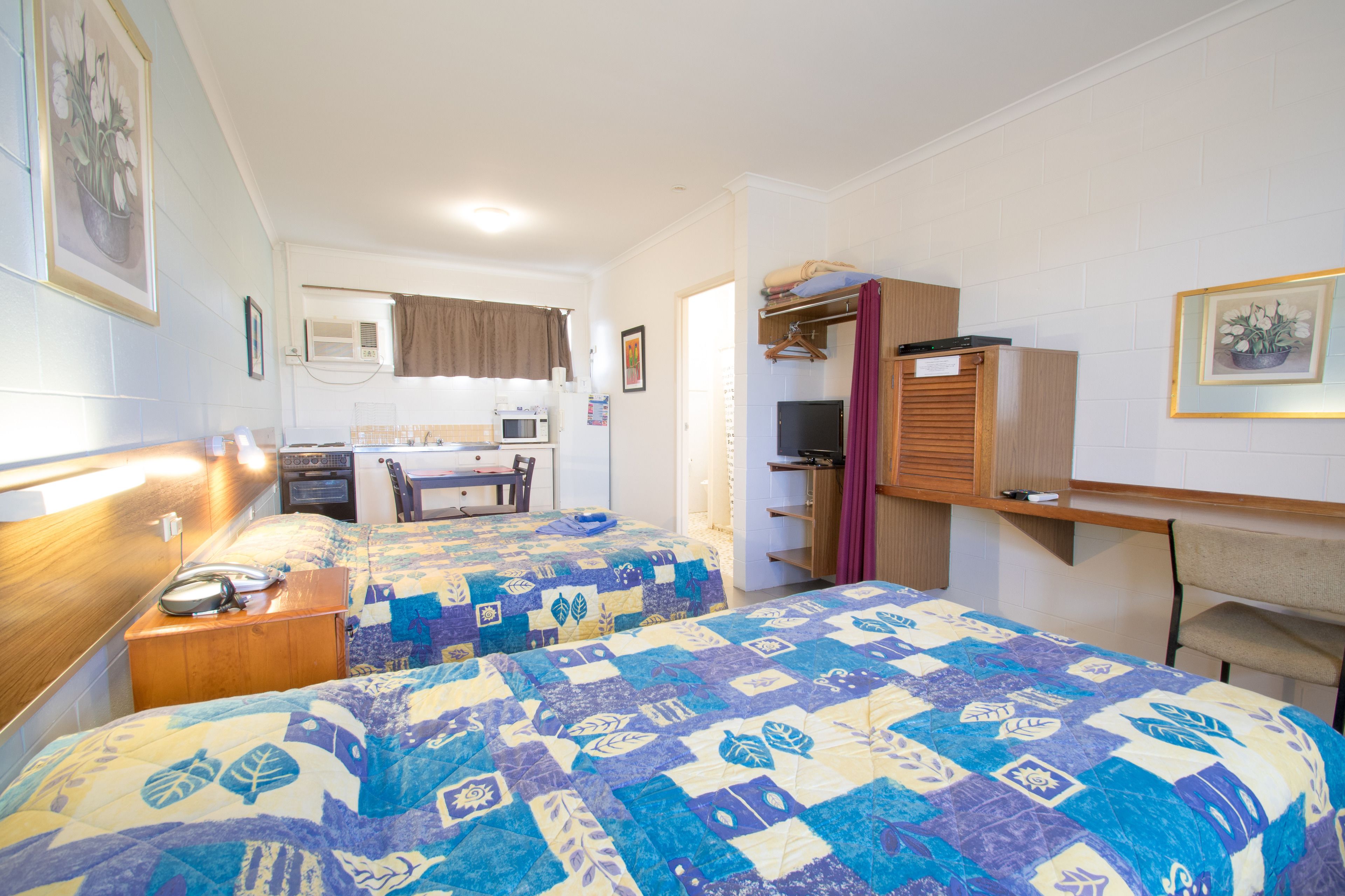 A bedroom with two beds, a desk, a chair, a wardrobe, and a kitchenette.