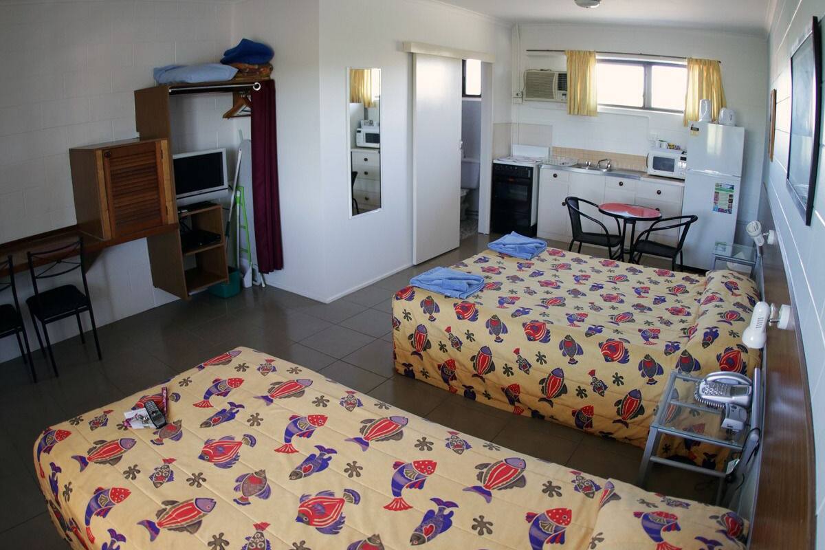 Une chambre d’hôtel compacte comprenant deux lits, un coin cuisine, un petit bureau et une chaise.