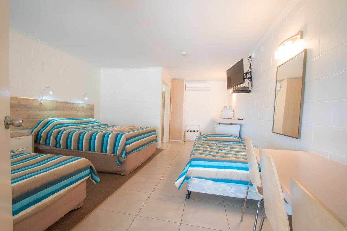 Une chambre d’hôtel avec deux lits, un bureau, une chaise, une télévision et un miroir.
