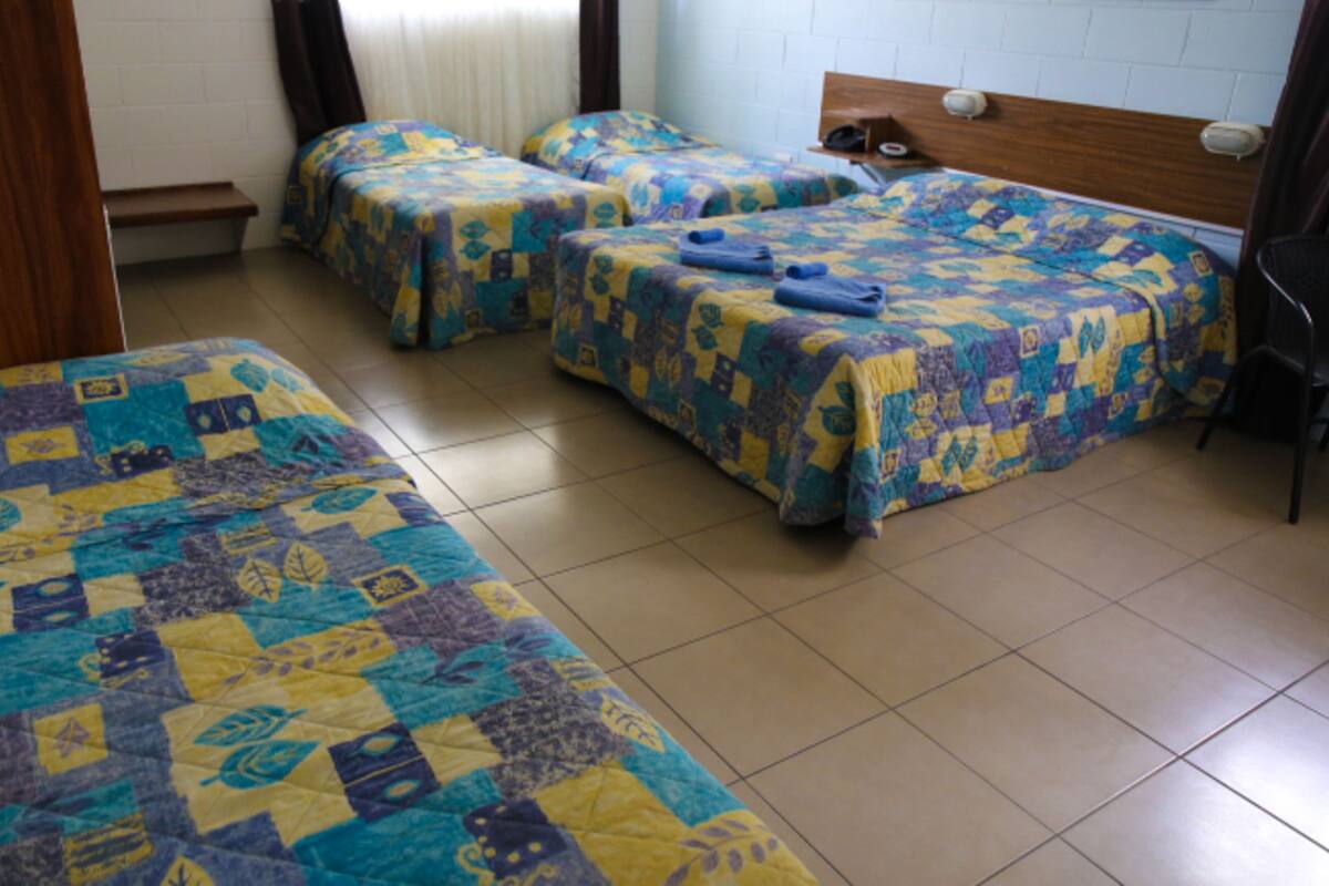 Une chambre avec trois lits, chacun recouvert d’une couvre-lit à motifs. Il y a un banc adossé au mur et une tête de lit en bois sur l’un des lits.