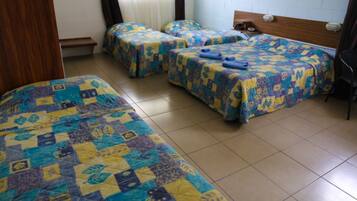 Une chambre avec trois lits, chacun recouvert d’une couvre-lit à motifs. Il y a un banc adossé au mur et une tête de lit en bois sur l’un des lits.