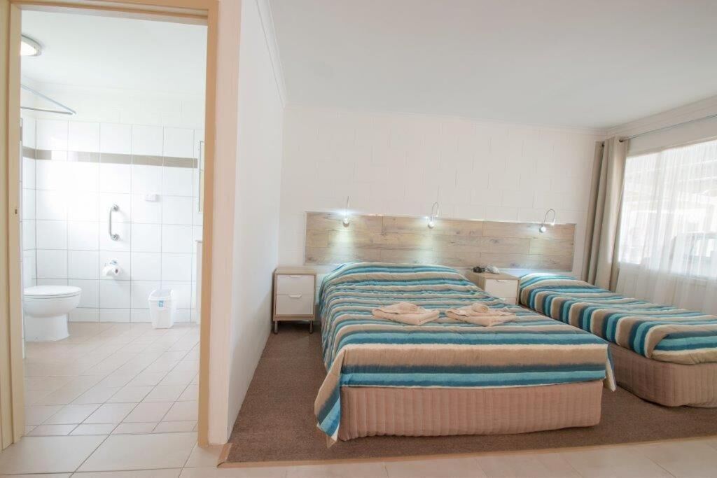 Quarto de hotel com uma cama grande, mesa de cabeceira, banheiro com vaso sanitário e chuveiro.
