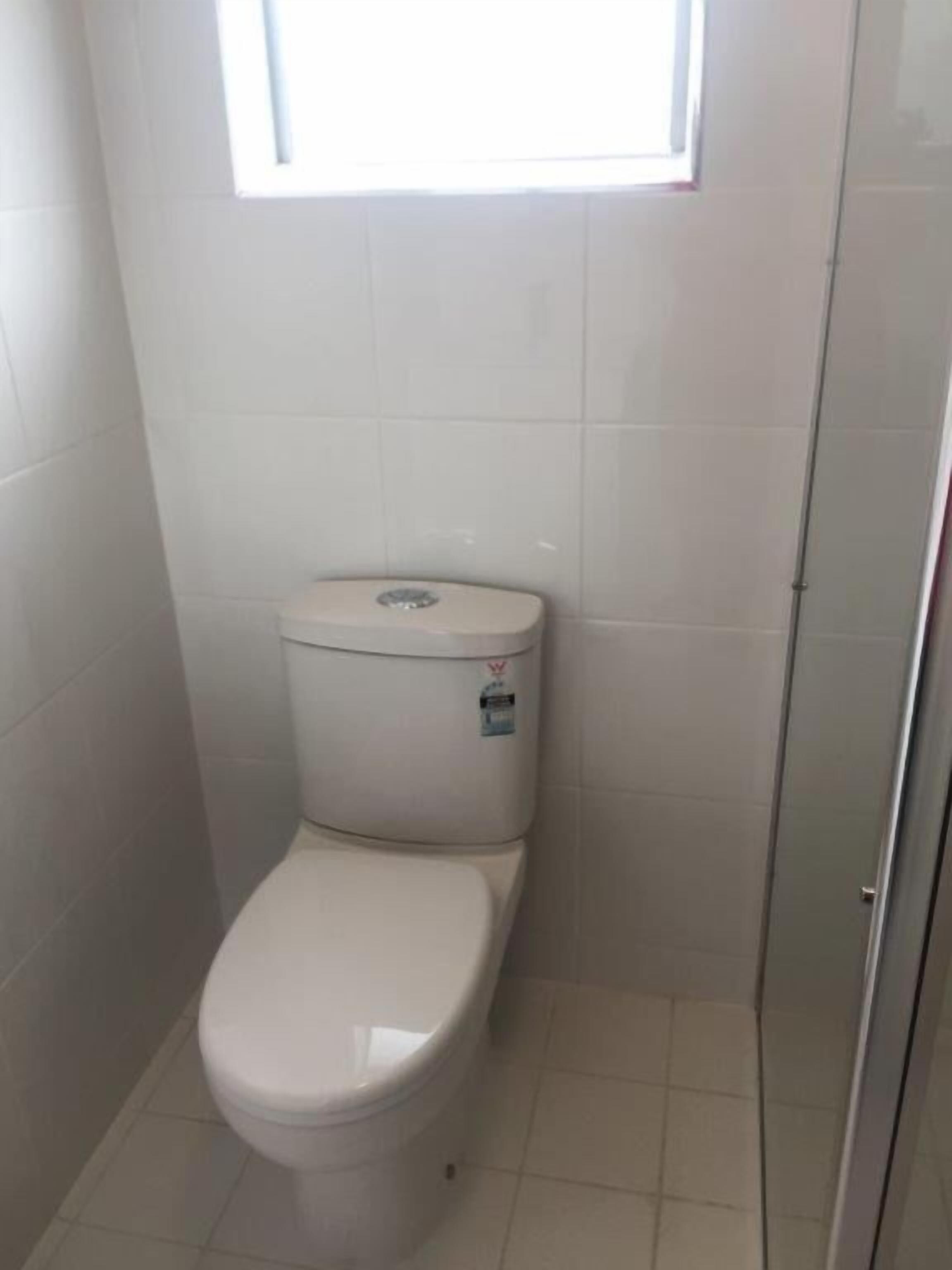 Ein kleines, weiß gefliestes Badezimmer mit Toilette und einem Fenster darüber.