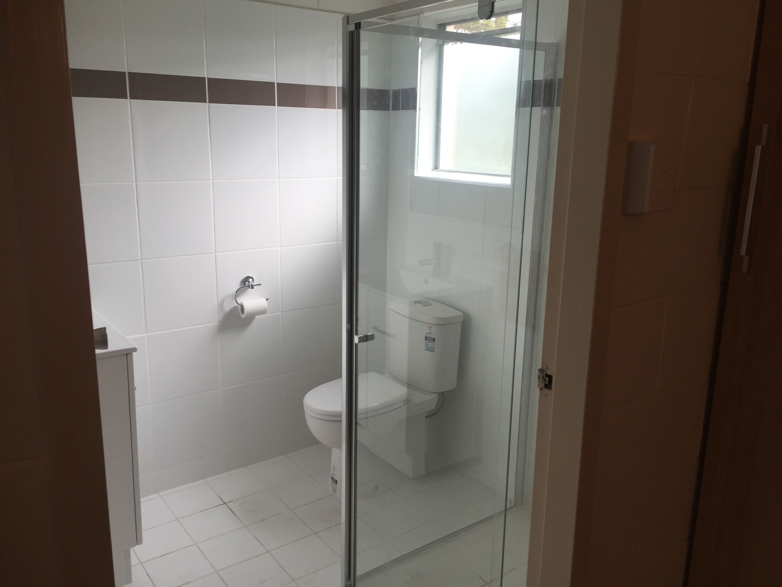 Un baño con cabina de ducha de vidrio, un inodoro y un rollo de papel higiénico en la pared.
