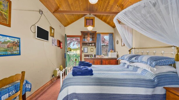 A bedroom with a large bed, a wooden ceiling, a window with a view, and a bedside table. - Sorell Barracks (Sorell)