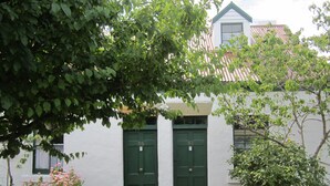 A white building with two green doors labeled B4 and B3, a brick pathway, and a garden with various plants. - Sorell Barracks (Sorell)