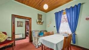 A dining room with a table set for four, a red chair, a patterned armchair, and a wooden ceiling. - Sorell Barracks (Sorell)