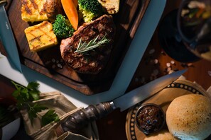 A wooden cutting board with a steak, roasted vegetables, and a knife.