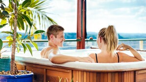 Una pareja en un jacuzzi con vistas al océano y a las montañas.