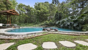 Piscina rodeada de abundante vegetación, con un porche de madera y escalones de piedra que conducen a ella.