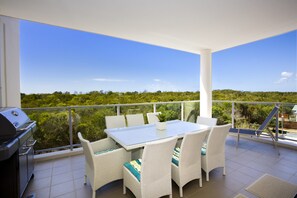 A balcony with a table and chairs, a grill, and a view of greenery.