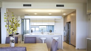 A modern kitchen with a central island, white cabinetry, and stainless steel appliances. - White Shells Luxury Apartments (Marcoola)