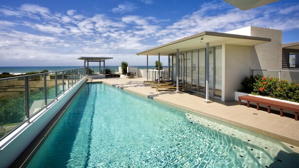 A modern infinity pool with a clear view of the ocean, a covered seating area, and a minimalist architectural design. - White Shells Luxury Apartments (Marcoola)